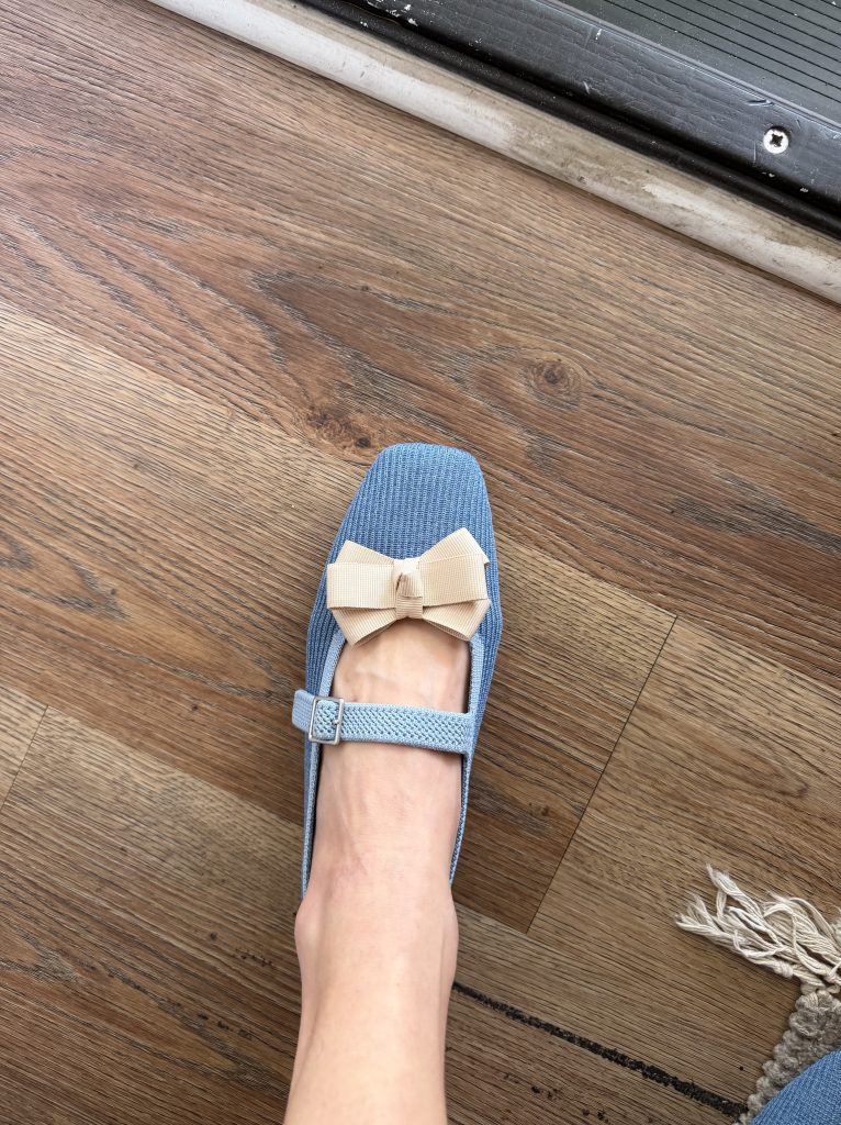 A blue knit Mary Jane shoe decorated with a cream bow.