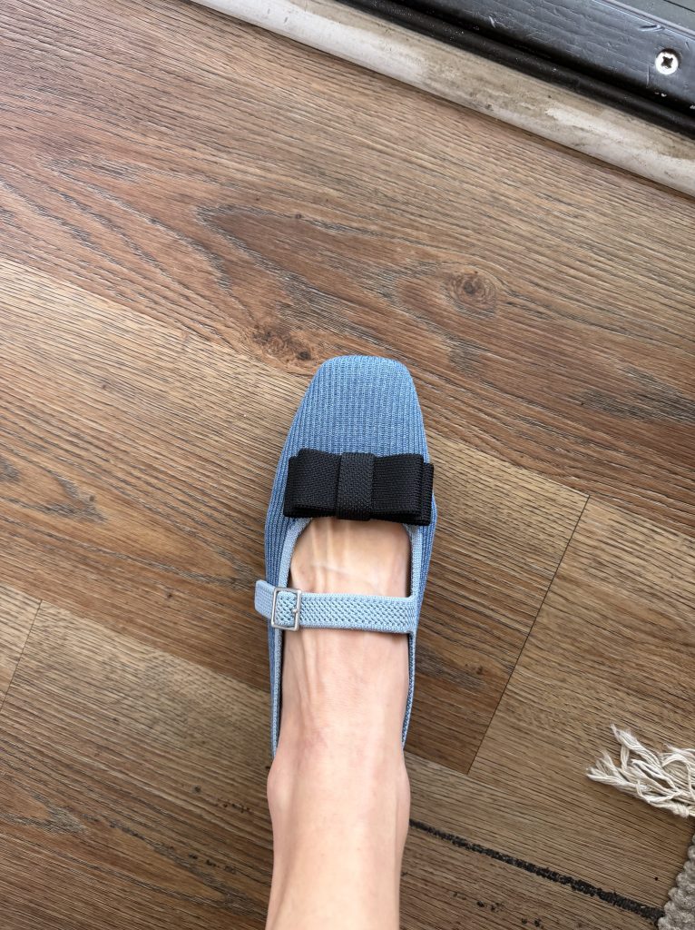A blue knit Mary Jane shoe decorated with a black bow.